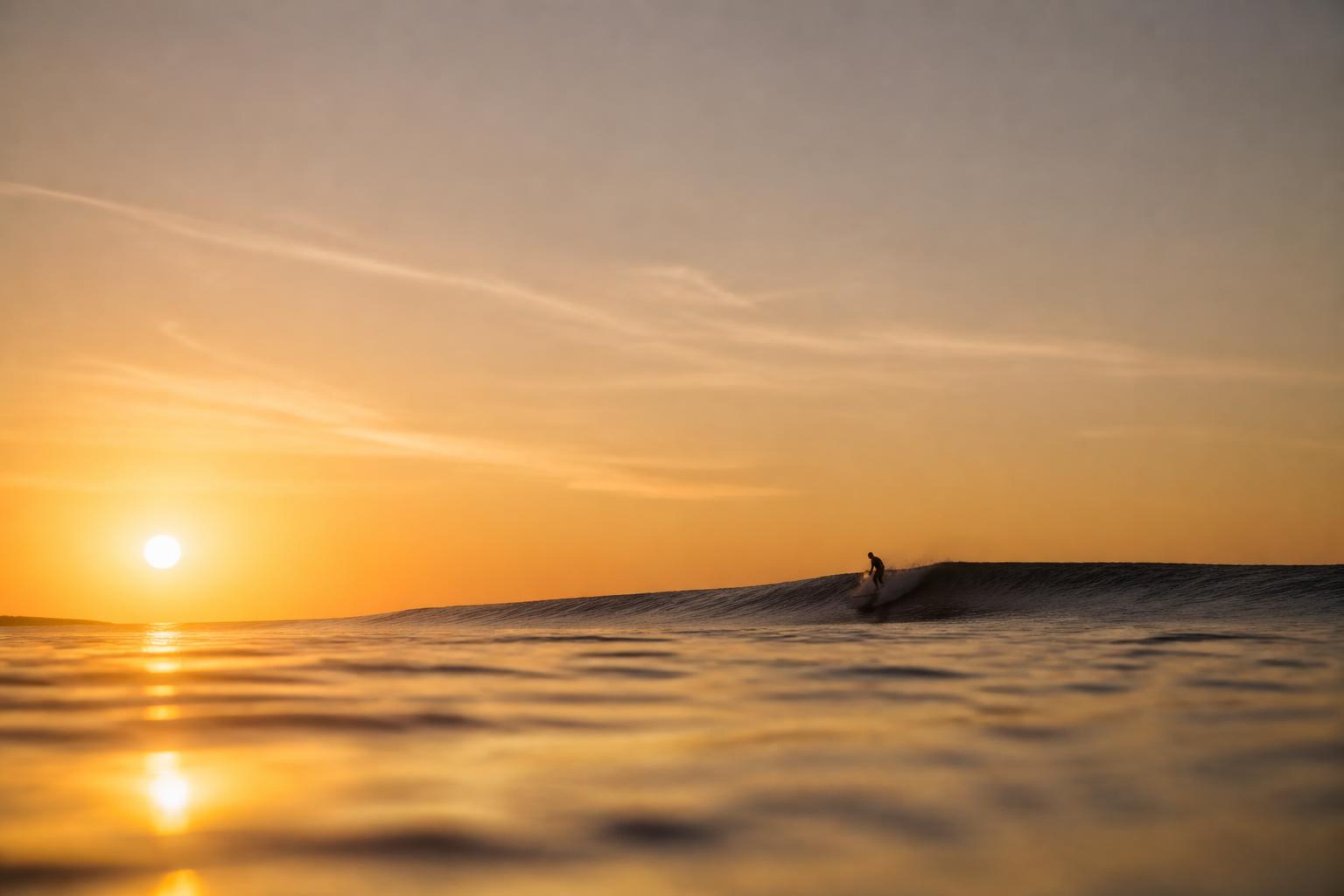 Ferne Silhouette einer surfenden Person bei Sonnenuntergang